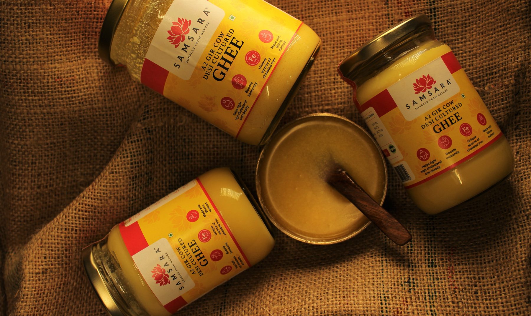 Overhead flat lay of Samsara ghee jars and a bowl of ghee on burlap