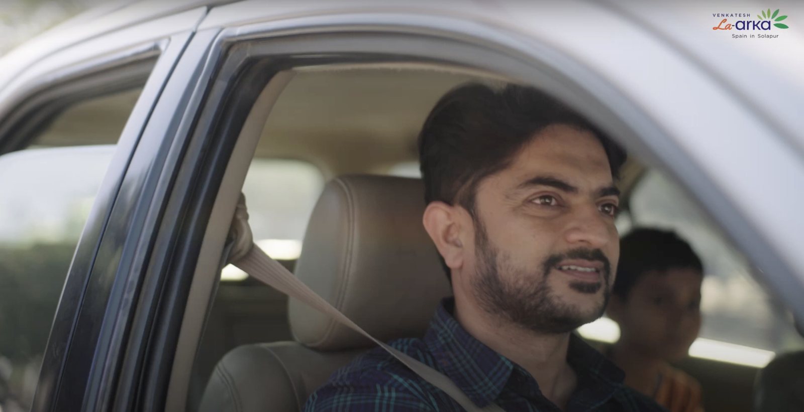 Still from the La Arka ad film: a man smiling at the wheel of a car