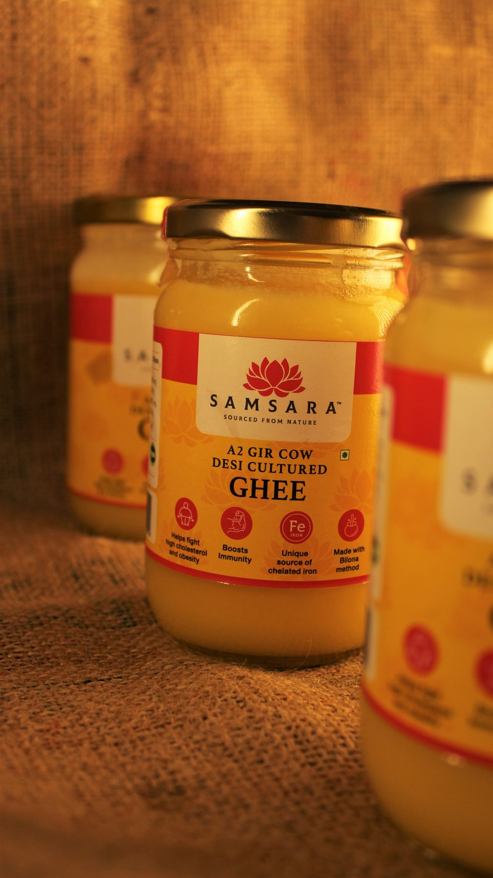 Three Samsara ghee jars lit warmly on burlap